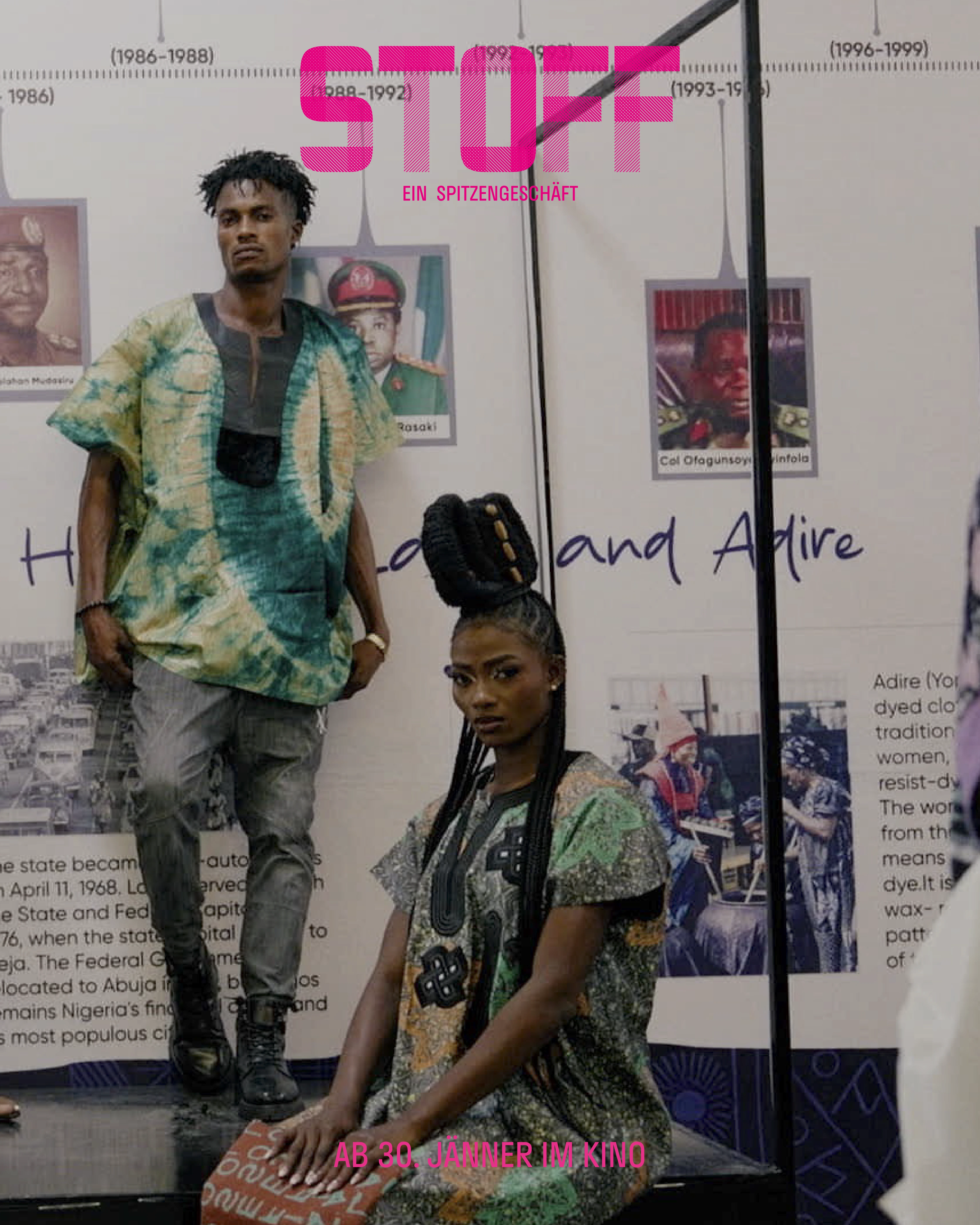 Zwei Models in traditioneller afrikanischer Kleidung auf einer Ausstellung mit historischen Porträts im Hintergrund.
